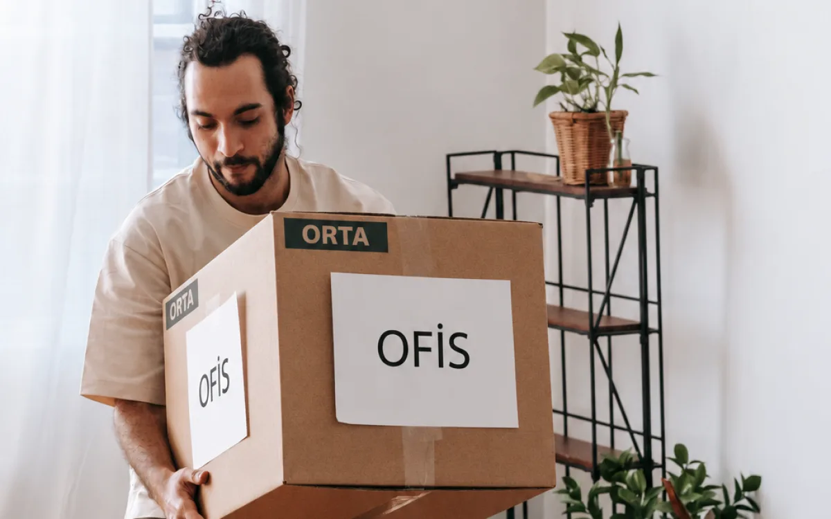 Ofis eşyaları için etiketlenmiş bir taşıma kolisini taşıyan kişi